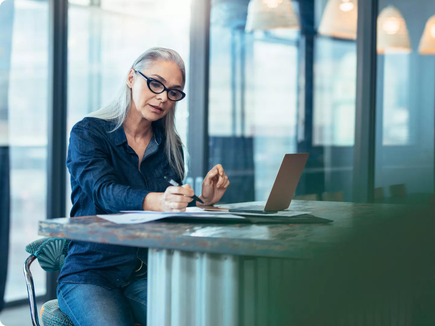 Woman going over information on a laptop and paperwork with a pen.
