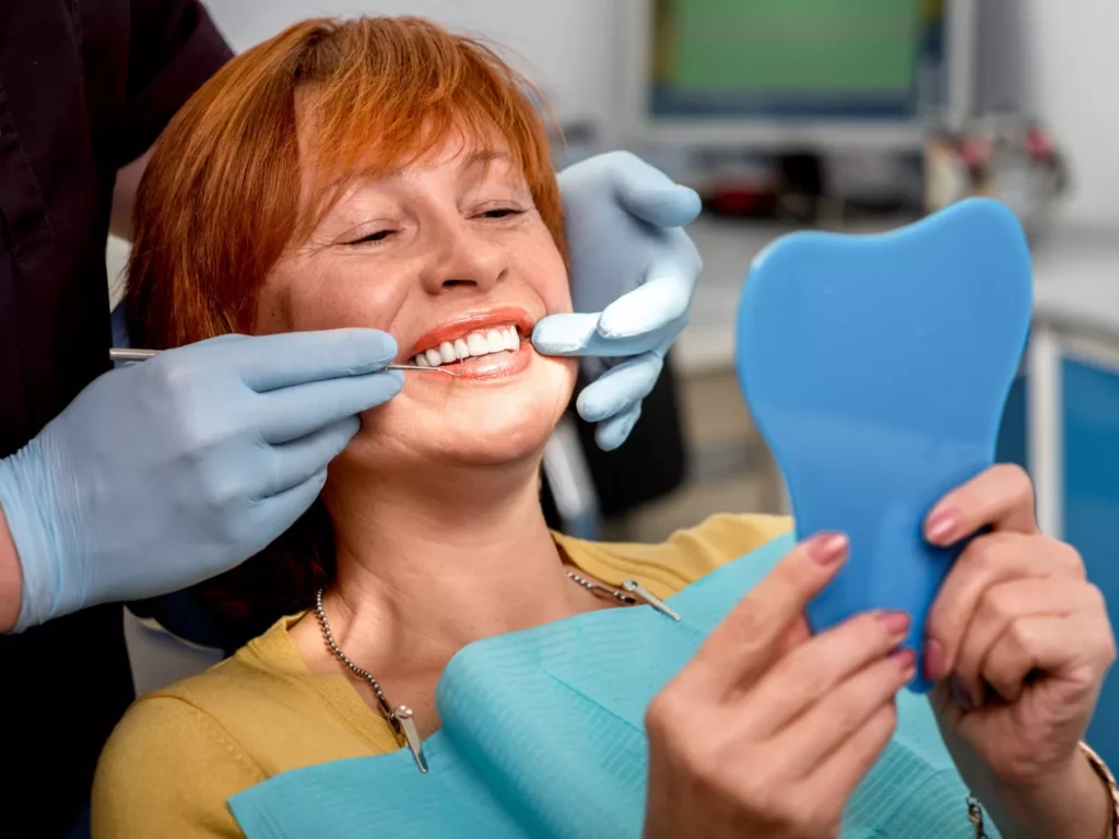 Woman smiling in a dental chair looking at her teeth in a mirror.